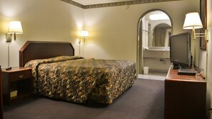 A hotel room with a bed, a desk with a computer, a mirror, and two wall-mounted lamps.