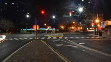 A nighttime street intersection with traffic lights, a pedestrian crossing, and a building with illuminated signage in the background.
