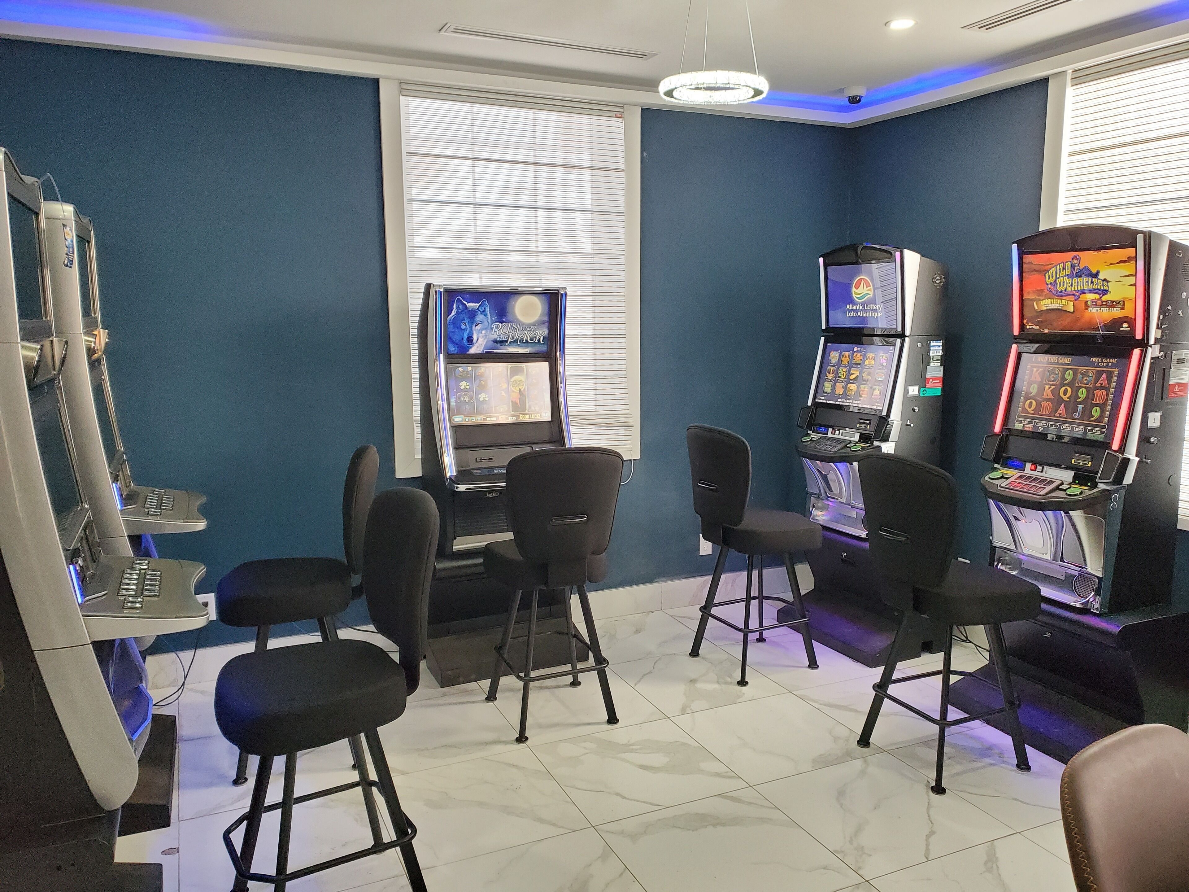 Zona de juegos con máquinas tragamonedas, una mesa con sillas y una pantalla grande mostrando un juego.