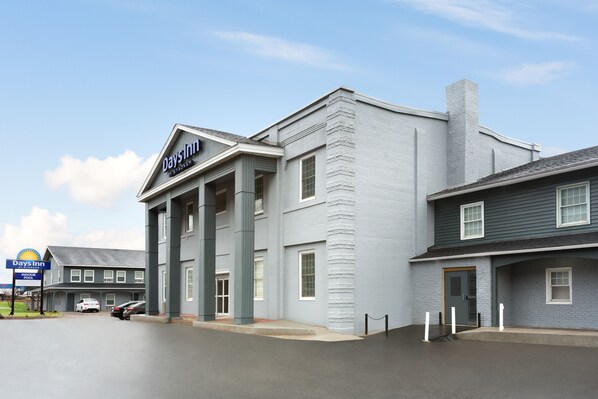 Edifício Days Inn com design moderno, destacando uma entrada imponente com colunas, amplo estacionamento e placa visível da piscina.