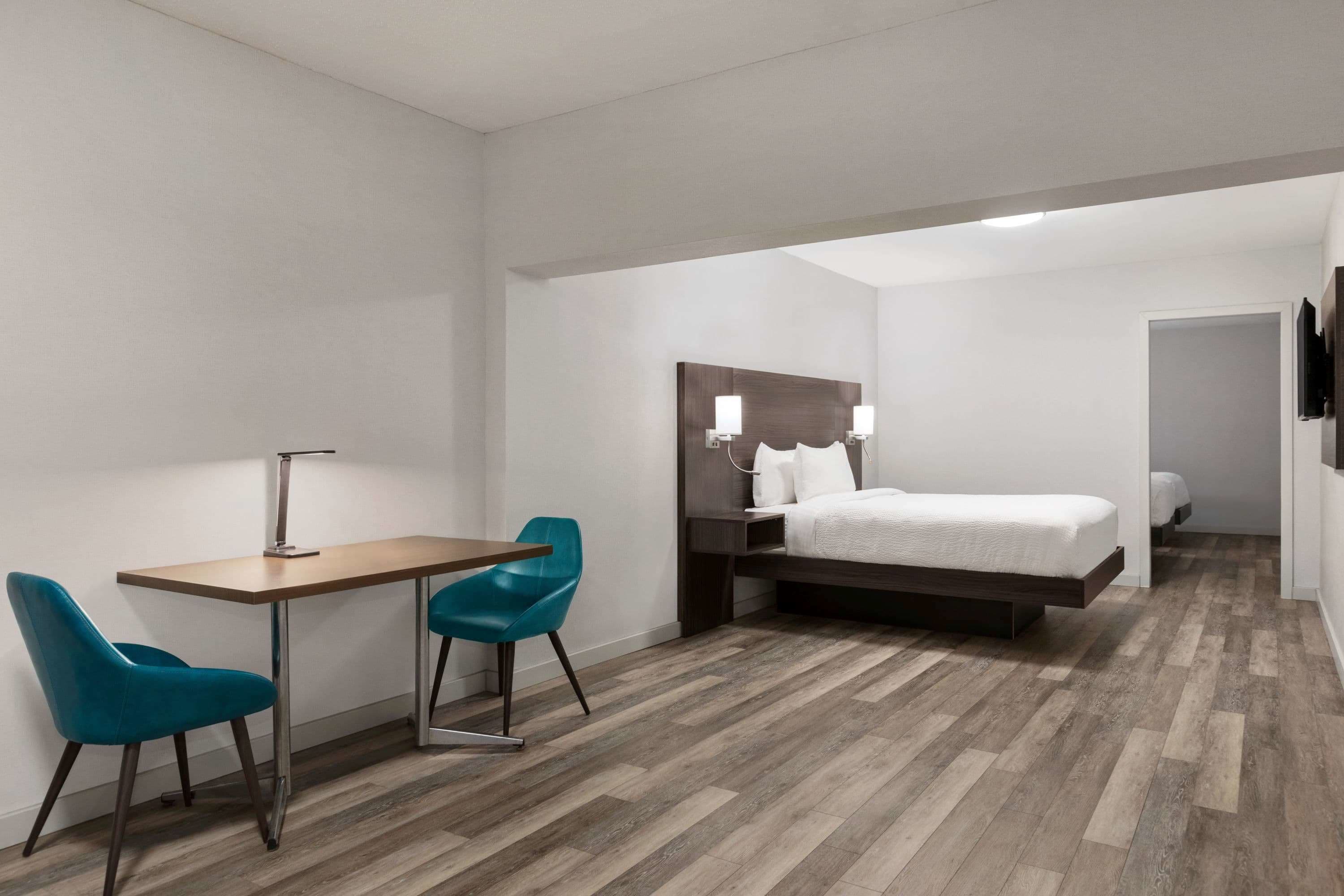 Habitación de hotel con cama, escritorio, dos sillas y mesita de noche con lámparas.