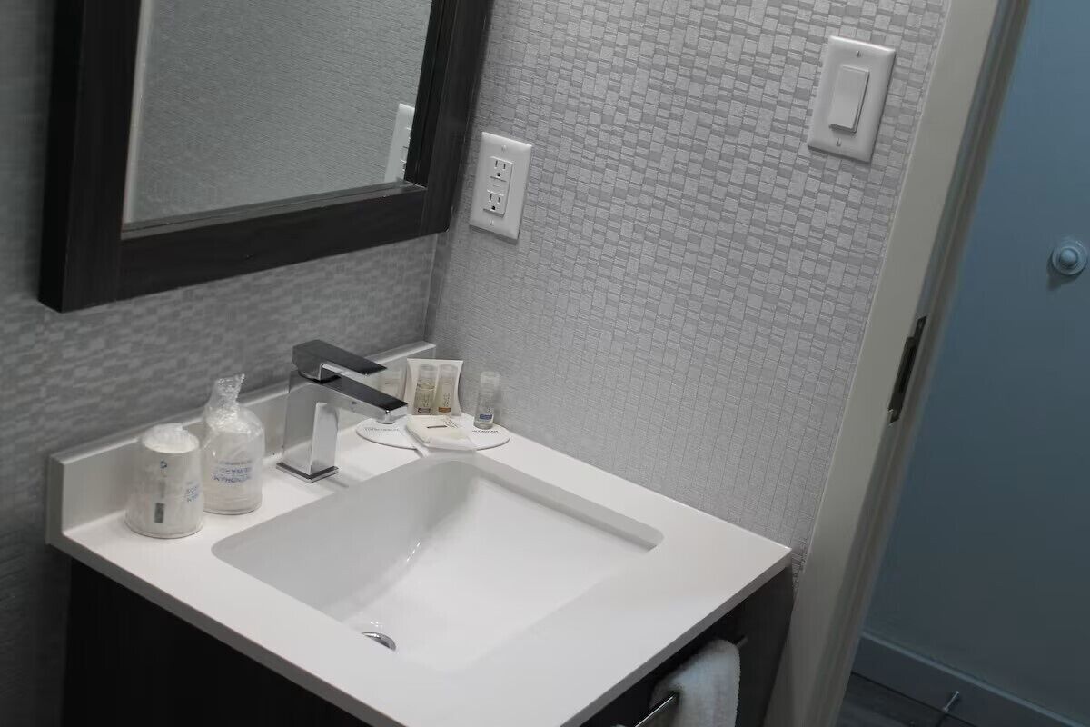 A bathroom with a white sink, a mirror, and toiletries on the counter.