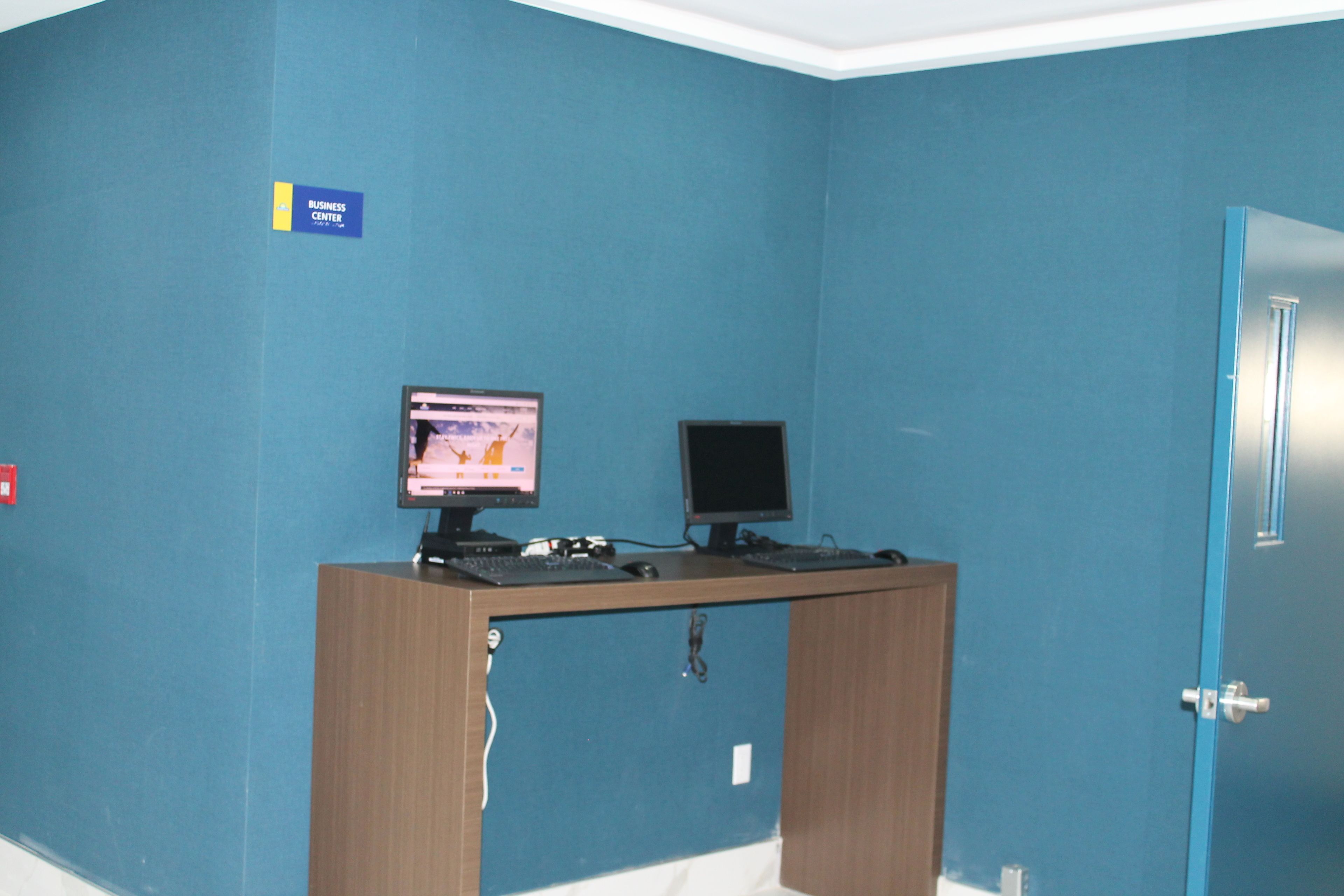 Een kamer met een blauwe wand, een houten bureau met twee schermen en een deur met een blauwe omlijsting.