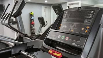 Una cinta de correr con pantalla digital y panel de control, en un gimnasio con otros equipos de ejercicio.