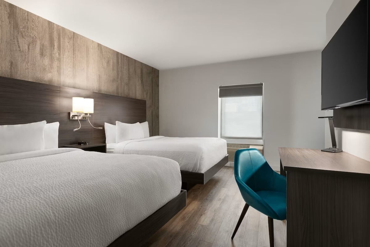 Ett hotellrum med två sängar, ett skrivbord, en stol, en TV och ett fönster med persienner.