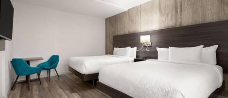 Habitación de hotel con dos camas, una mesita pequeña, dos sillas y un televisor.