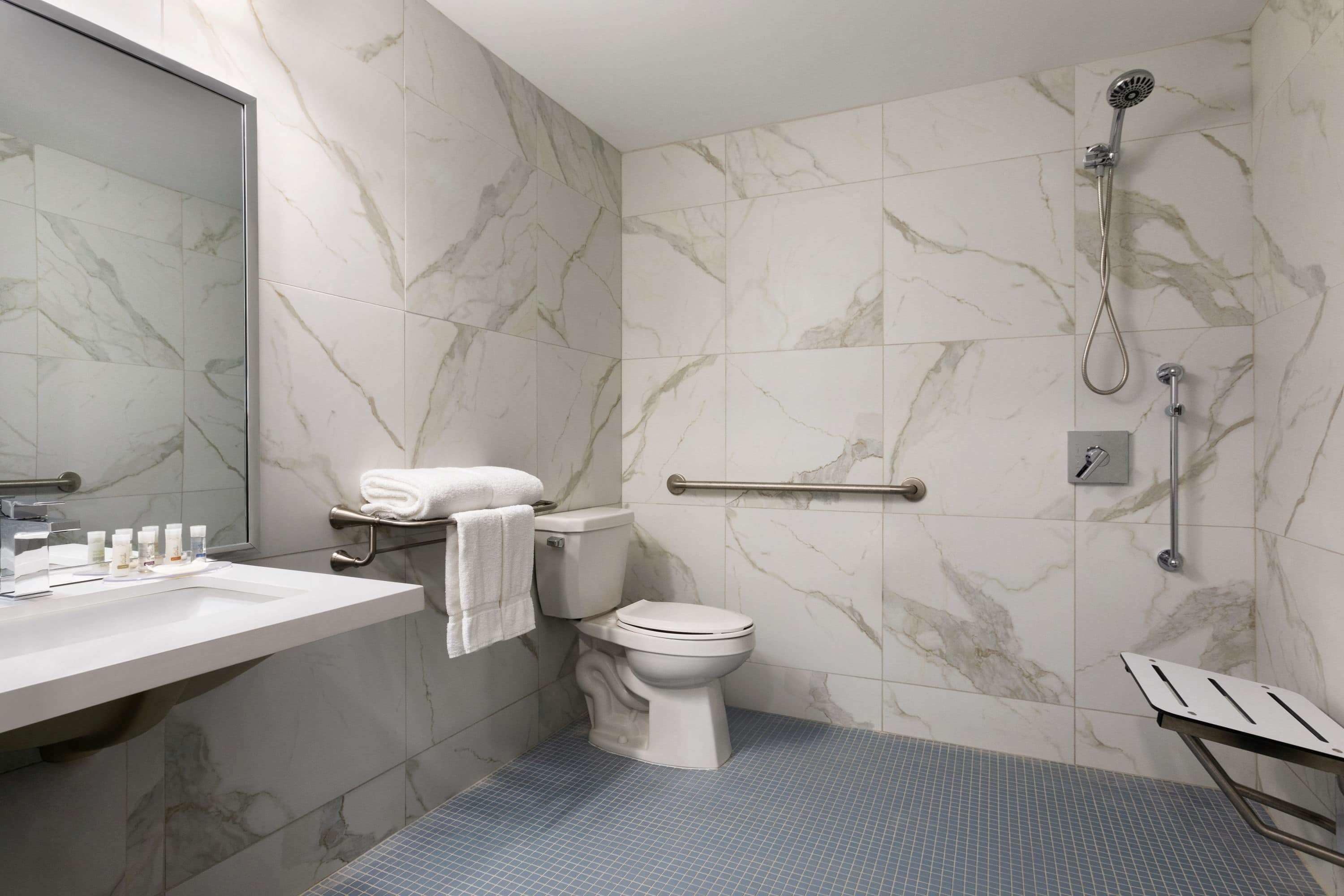 A bathroom with a marble wall, a white toilet, a sink with toiletries, and a shower area.