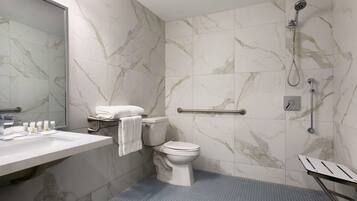 A bathroom with a marble wall, a white toilet, a sink with toiletries, and a shower area.