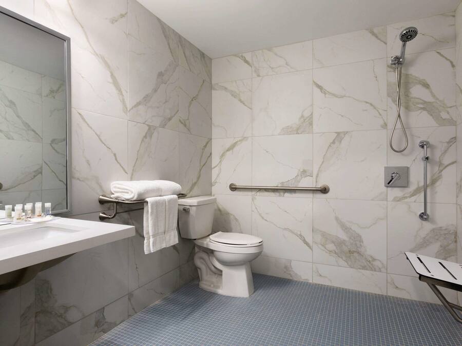 A bathroom with a marble wall, a white toilet, a sink with toiletries, and a shower area.
