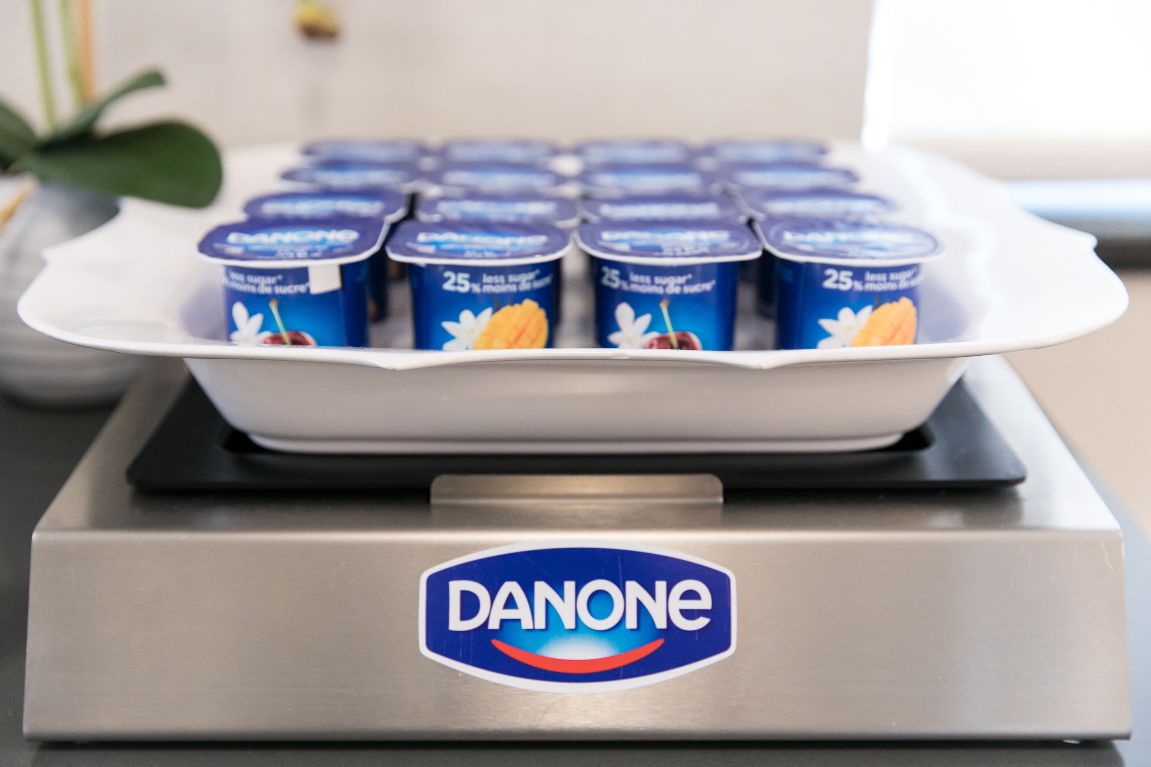 A stainless steel appliance with a label reading "DANONE" and a tray containing multiple yogurt containers.
