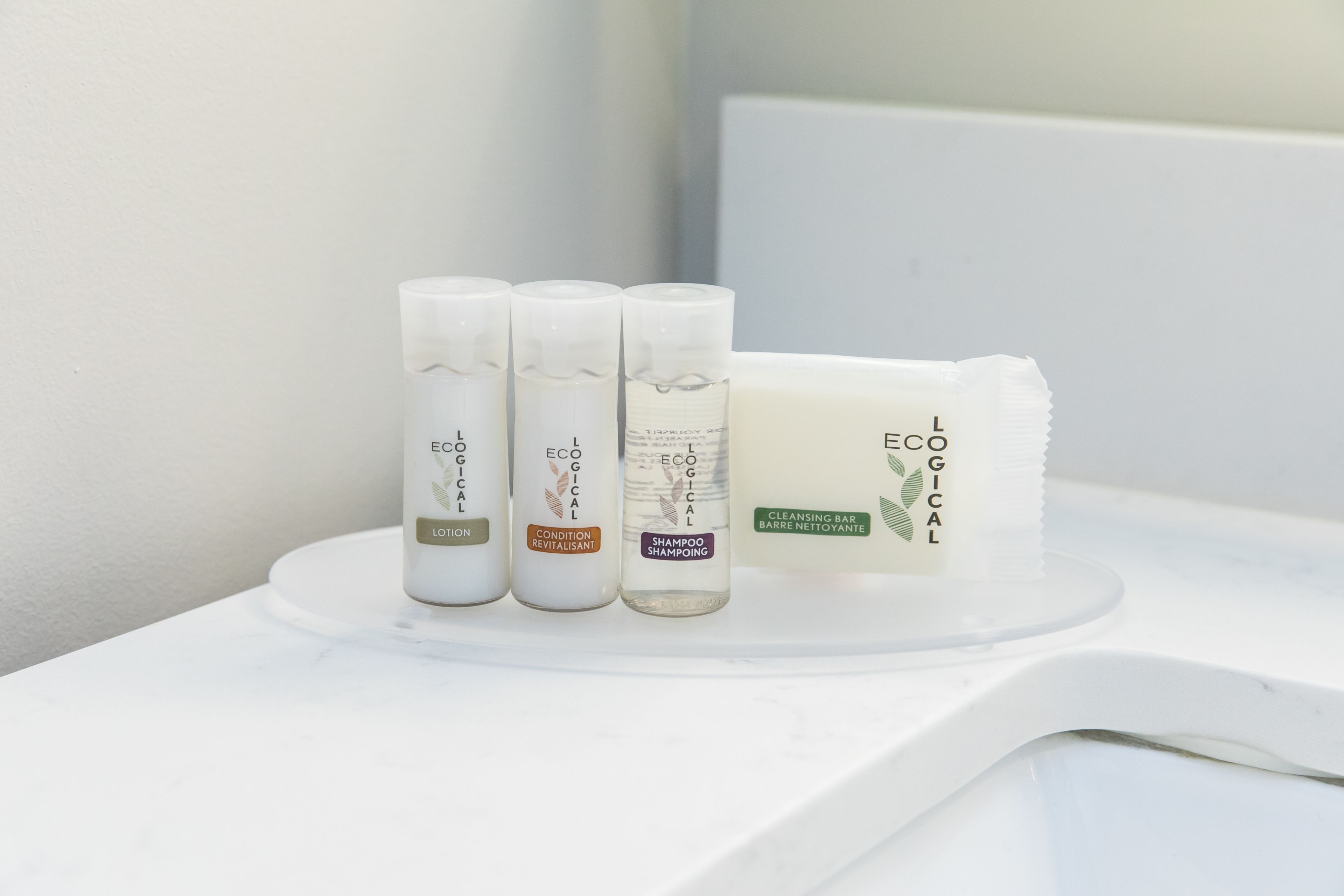A bathroom with a white countertop displaying three bottles of L'ECOLYGE products and a bar of soap.