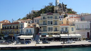 A coastal hotel with multiple floors, balconies, and a prominent clock tower. - Manessi City Hotel (Poros)