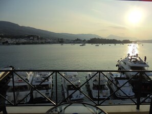 A marina with multiple boats docked, a clear view of the water, and a distant cityscape with mountains. - Manessi City Hotel (Poros)