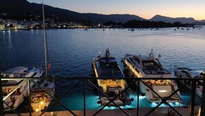 A marina at dusk with several yachts docked, a clear view of the water, and a distant cityscape. - Manessi City Hotel (Poros)