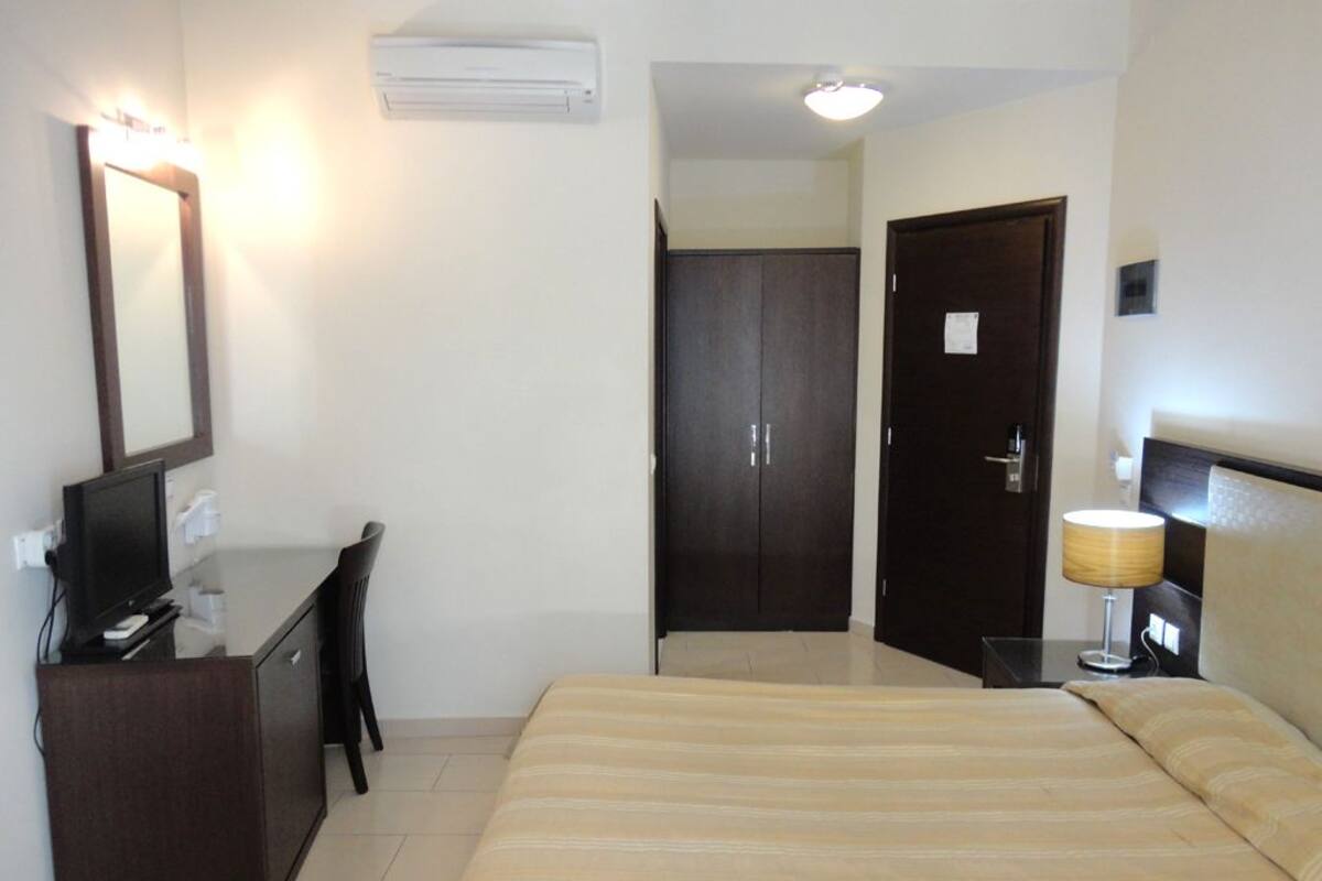 A hotel room with a bed, a desk with a computer, a mirror, a wardrobe, and a lamp.