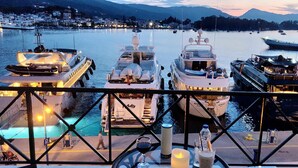 A marina with several yachts docked, a pedestrian walkway, and a table with drinks and a candle. - Manessi City Hotel (Poros)