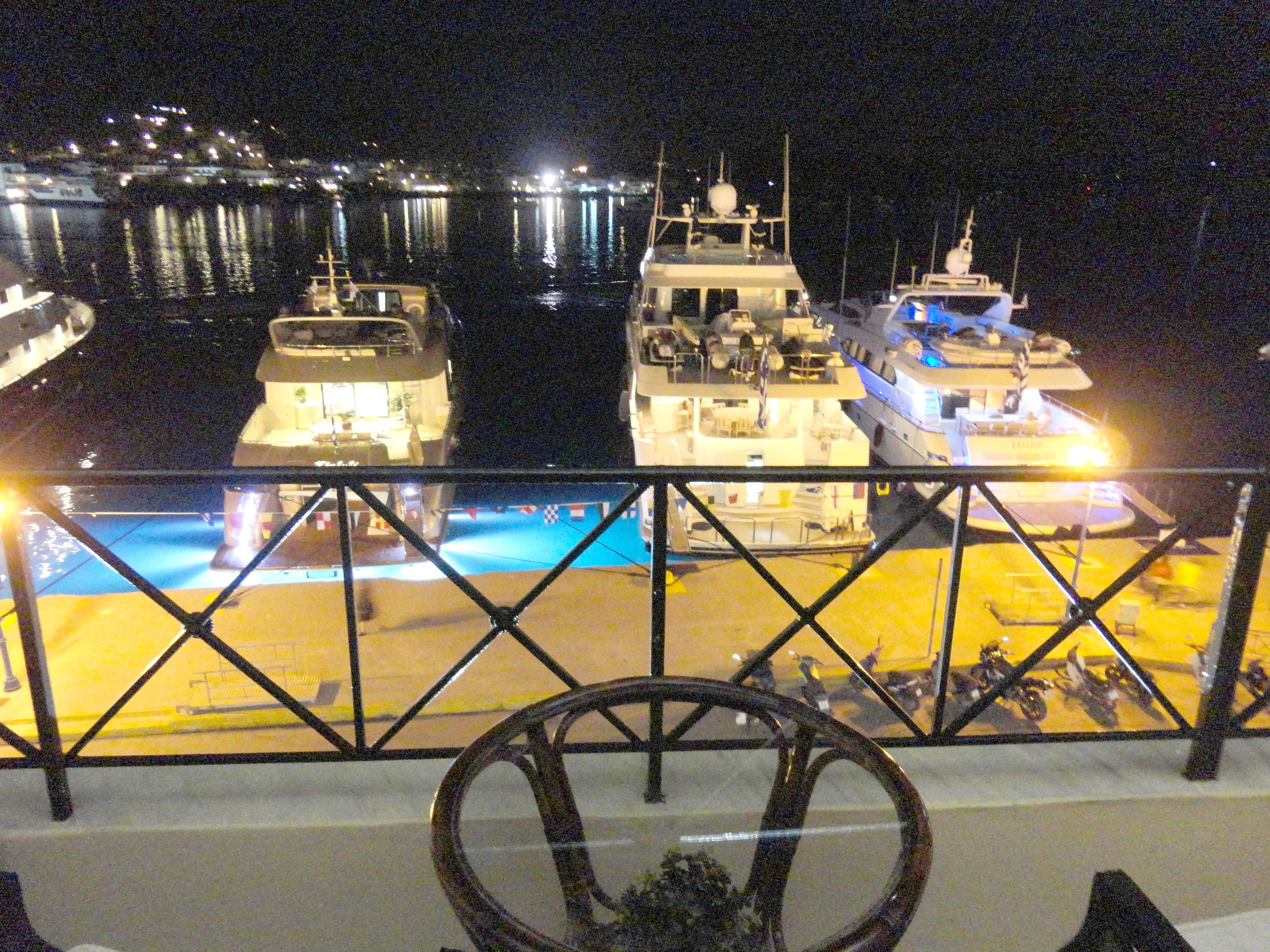 Un port de plaisance de nuit, avec des bateaux amarrés, un espace piscine et une rambarde au premier plan.