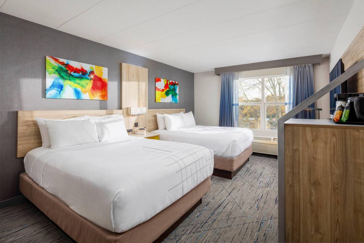 A hotel room with two beds, a desk, and a window with curtains.