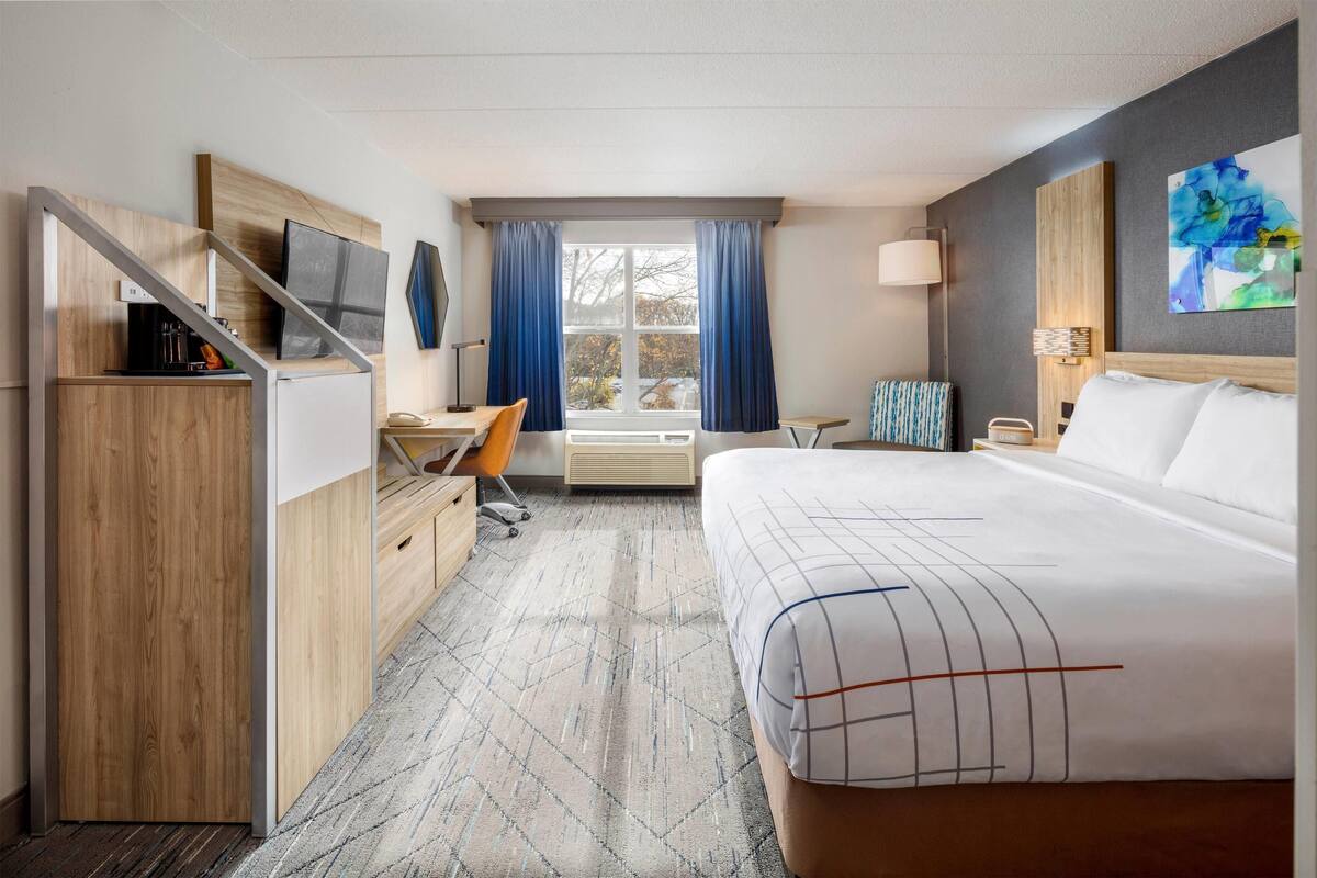 A hotel room with a bed, desk, chair, and a TV on a wooden cabinet.