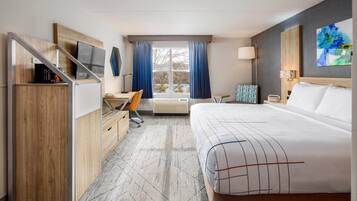 Habitación de hotel con cama, escritorio, silla y televisor sobre un mueble de madera.