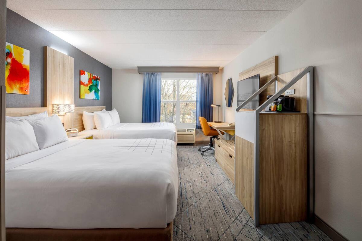 A hotel room with two beds, a desk, a chair, a wardrobe, and a window with curtains.