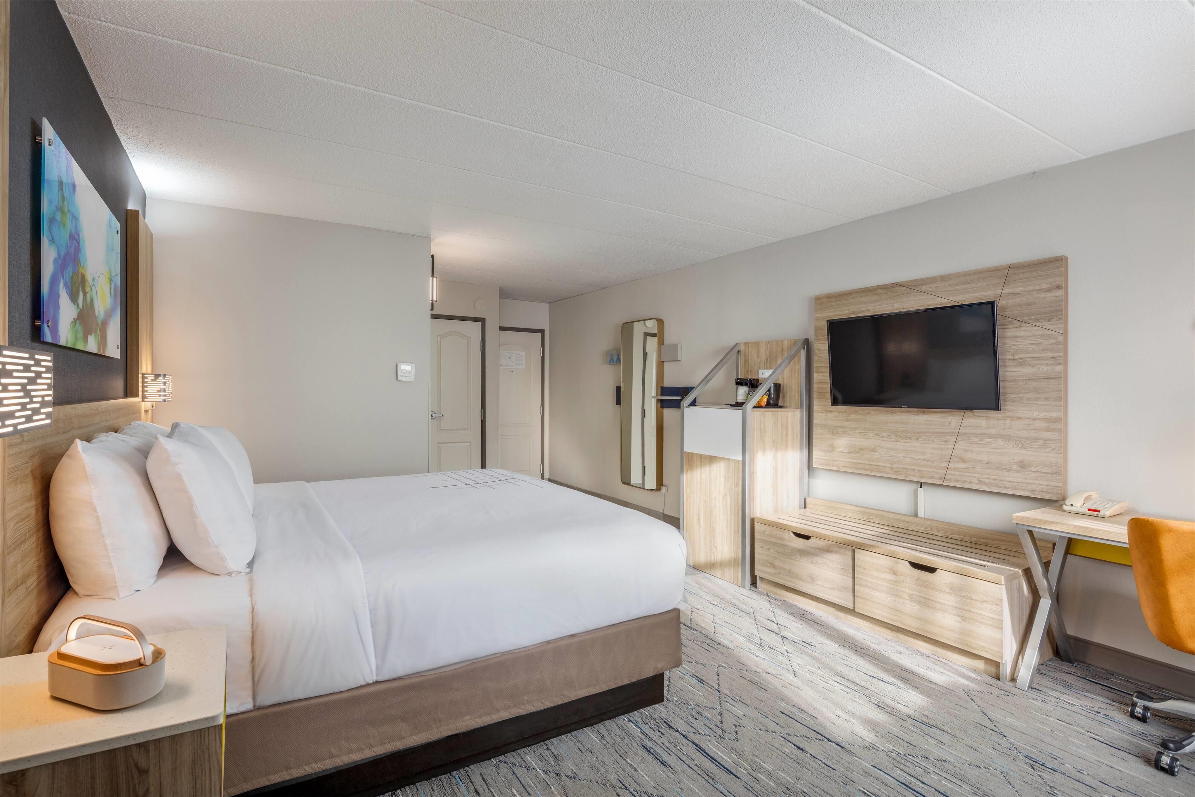 Una habitación de hotel moderna con una cama grande, un escritorio, una silla, un televisor y un cuadro en la pared.