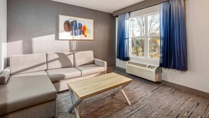 Una sala de estar moderna con un sofá seccional, una mesa de centro de madera, un cuadro abstracto enmarcado, una ventana con cortinas azules y un aire acondicionado instalado en la pared.