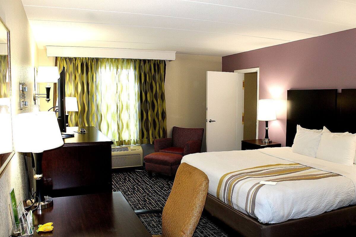 A hotel room with a bed, desk, chair, and a window with curtains.