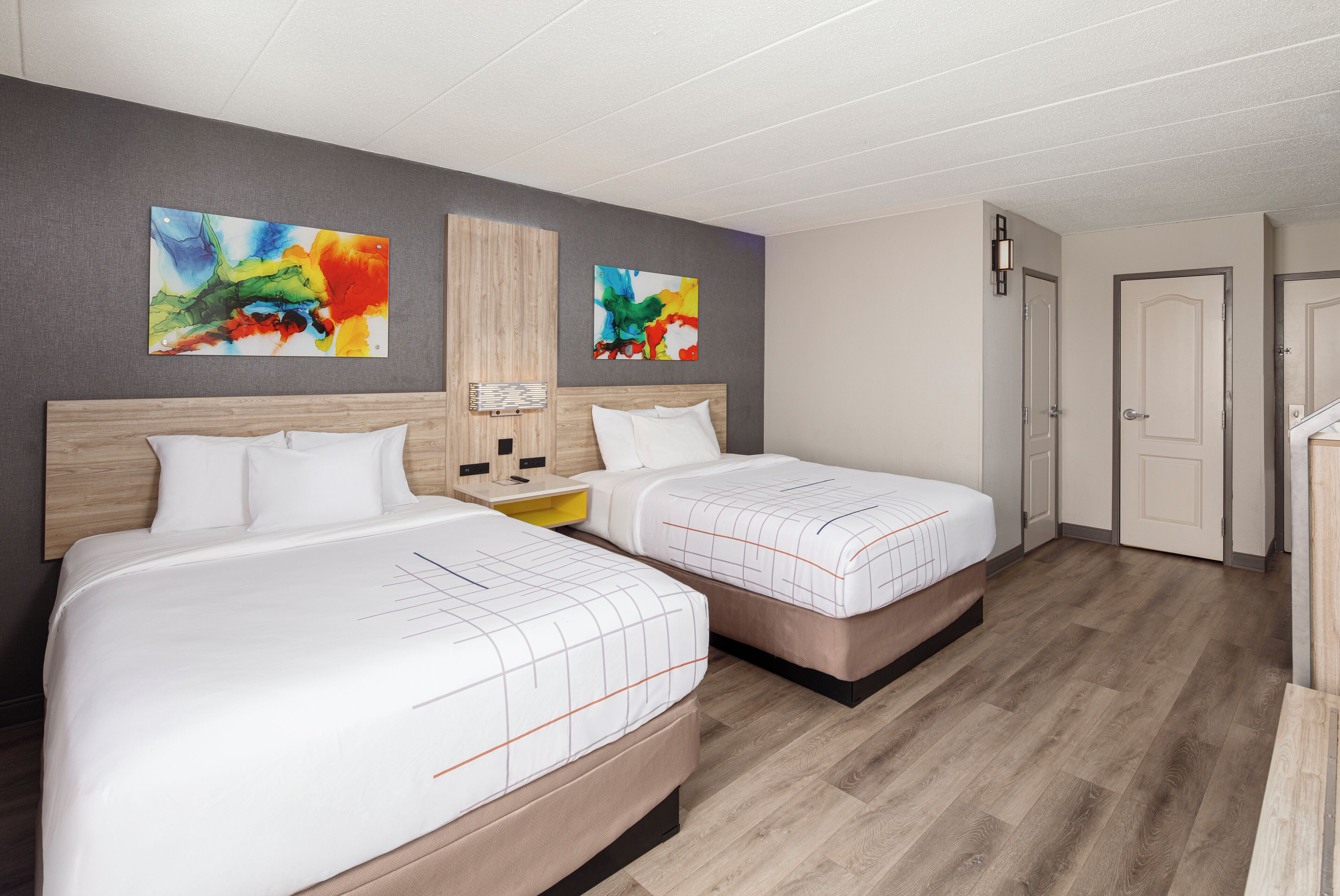 A hotel room with two beds, a wooden headboard, a nightstand, and abstract art on the wall.