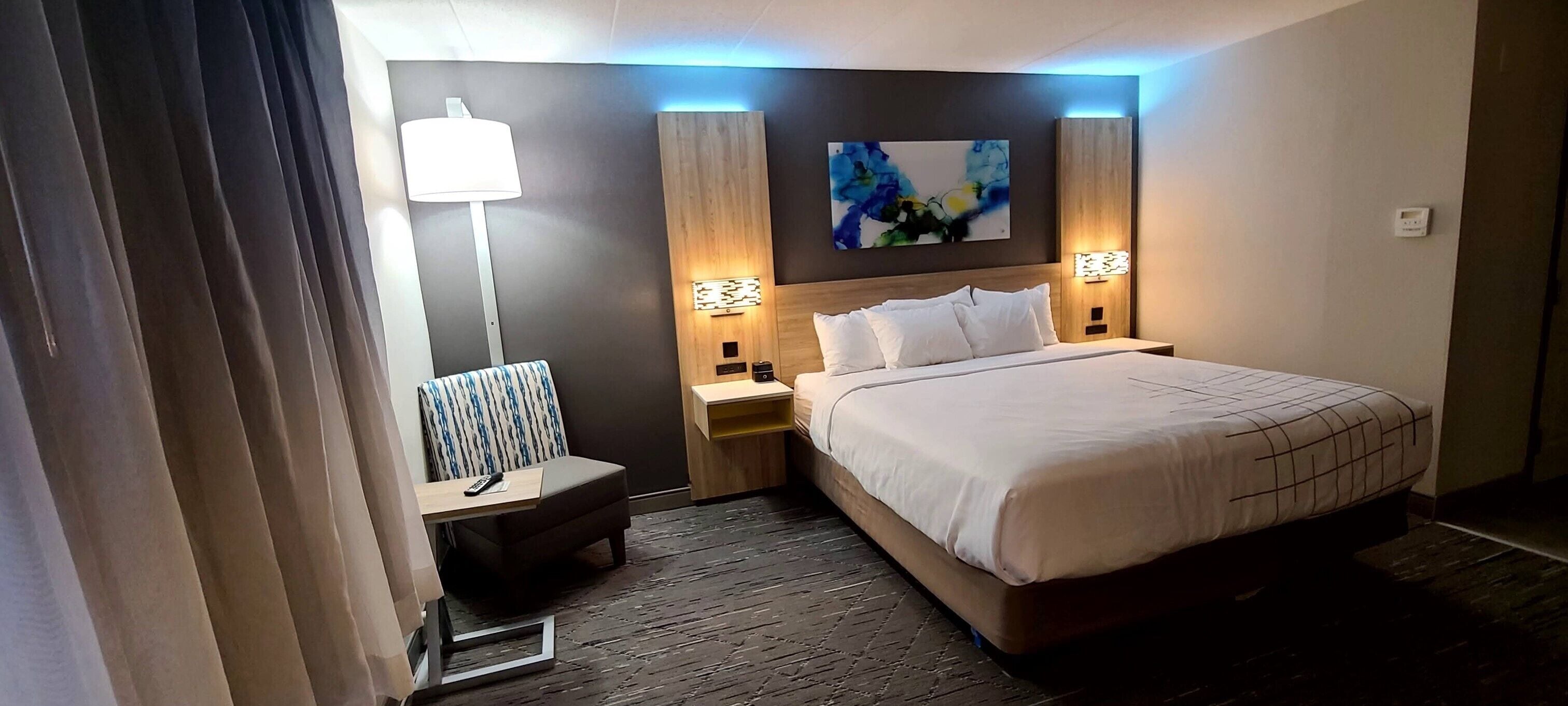 A hotel room with a bed, bedside tables, a lamp, a painting on the wall, and a curtain.