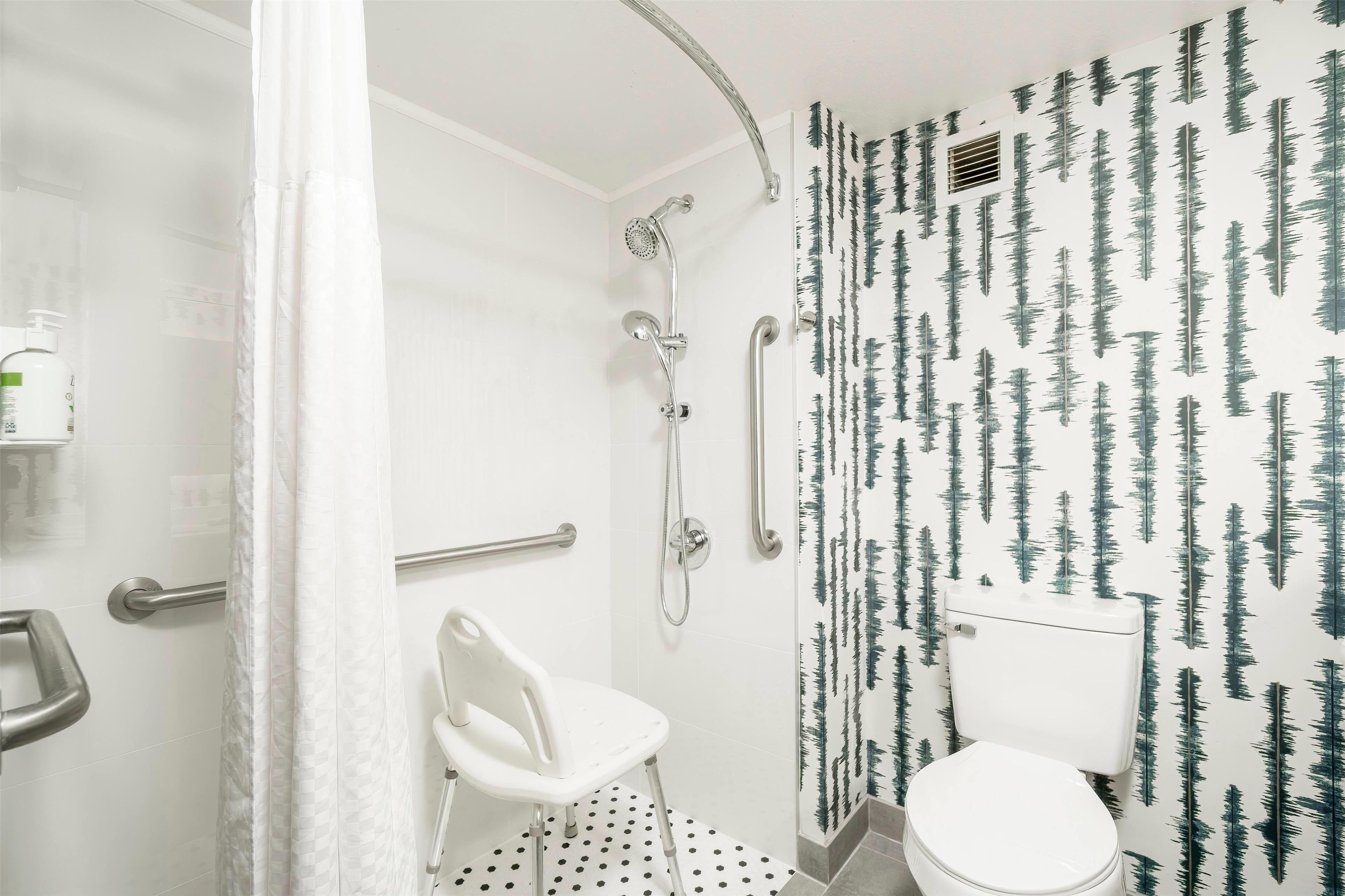 A bathroom with a shower, toilet, and a white chair.