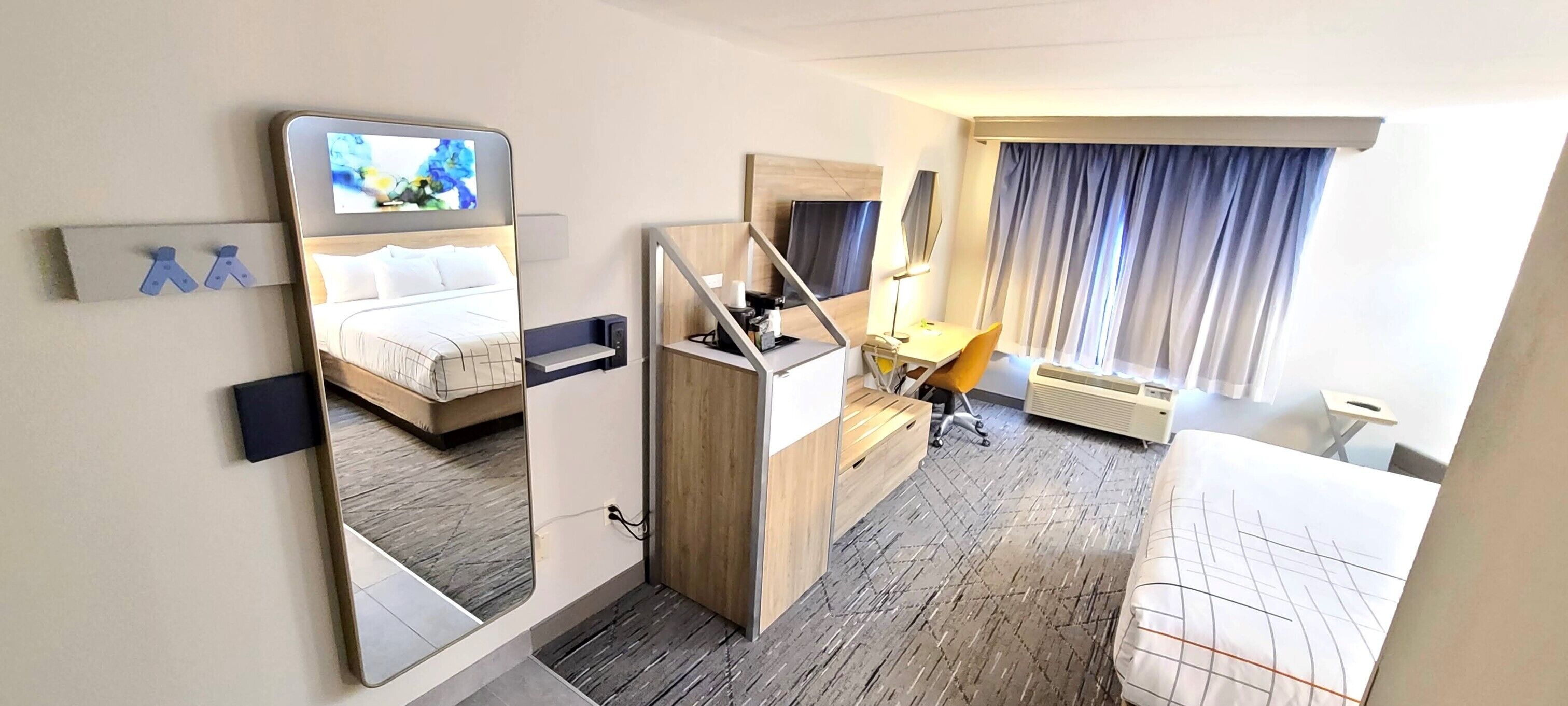 A hotel room with a bed, a desk, a chair, a TV, and a window with curtains.