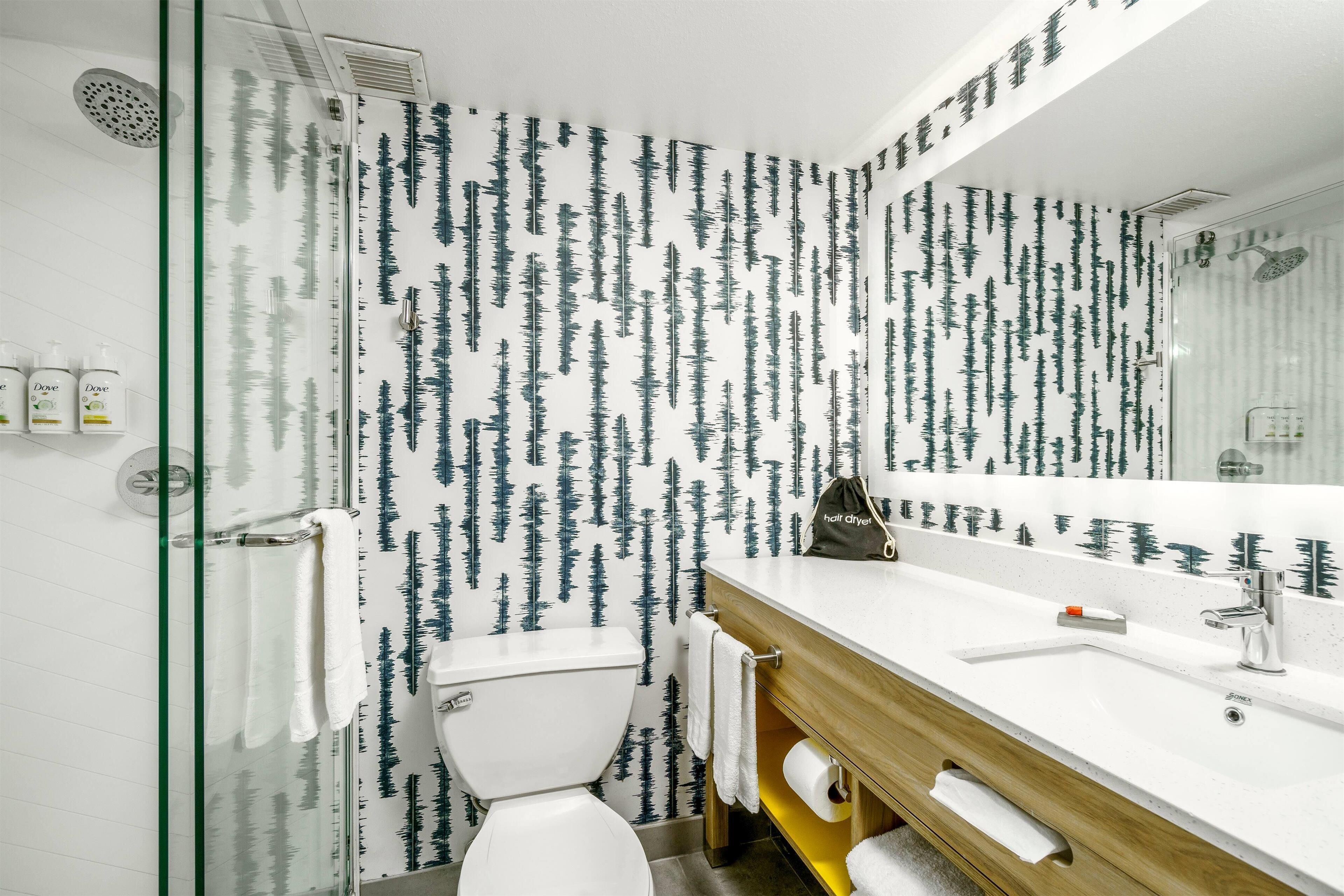 A modern bathroom with a glass shower enclosure, a white toilet, and a wooden vanity with a large mirror.