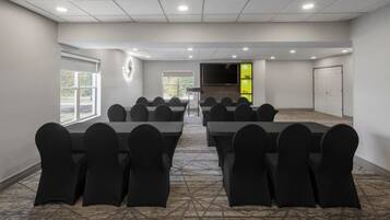 A conference room with multiple tables and chairs, a large screen, and a door with a green accent.