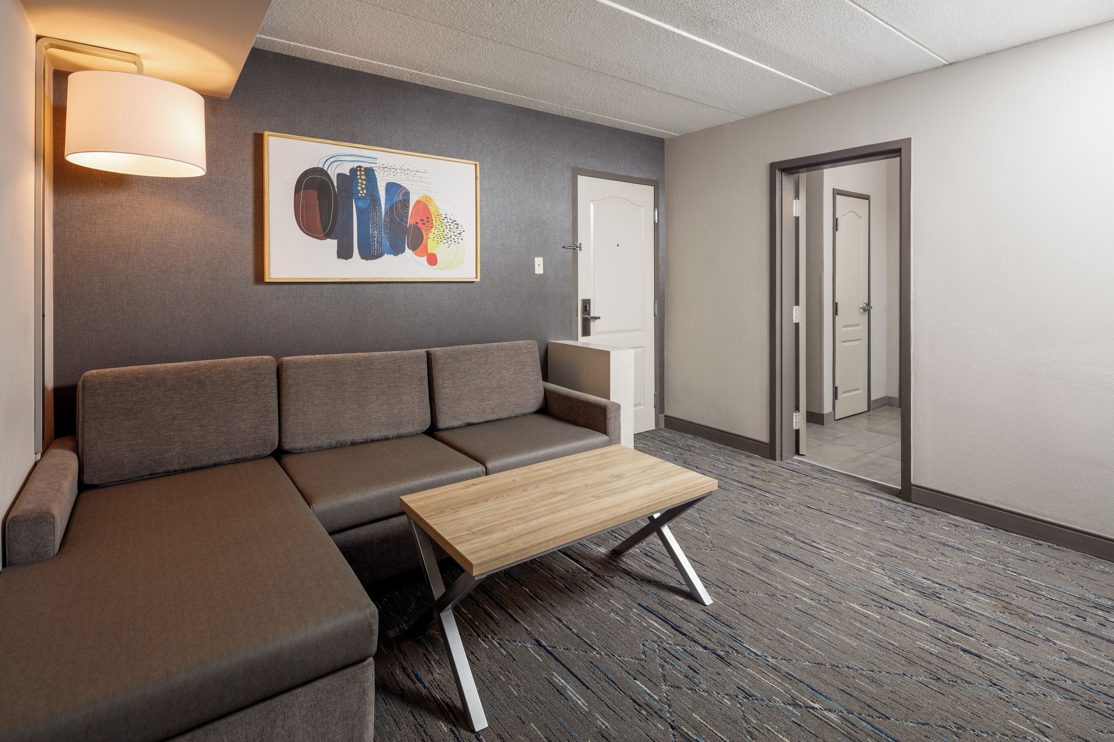 A modern office space with a grey sofa, a wooden coffee table, a framed abstract artwork, and a carpeted floor.