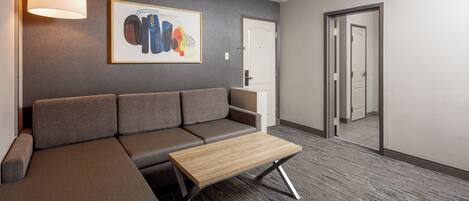 A modern office space with a grey sofa, a wooden coffee table, a framed abstract artwork, and a carpeted floor.