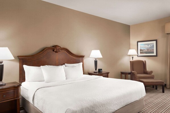 Una habitación de hotel con una cama grande, dos mesitas de noche, una silla y una lámpara.