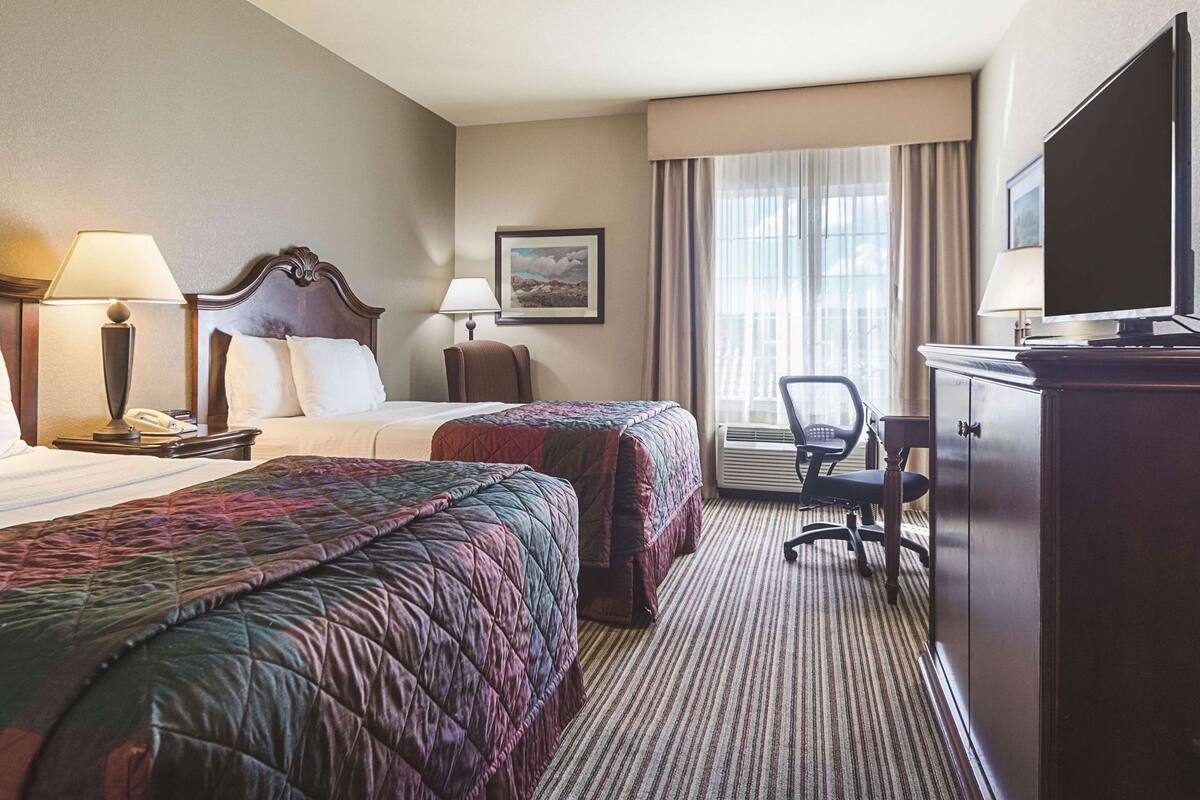 Hotelkamer met twee bedden, een bureau, een stoel, een televisie en een raam met gordijnen.