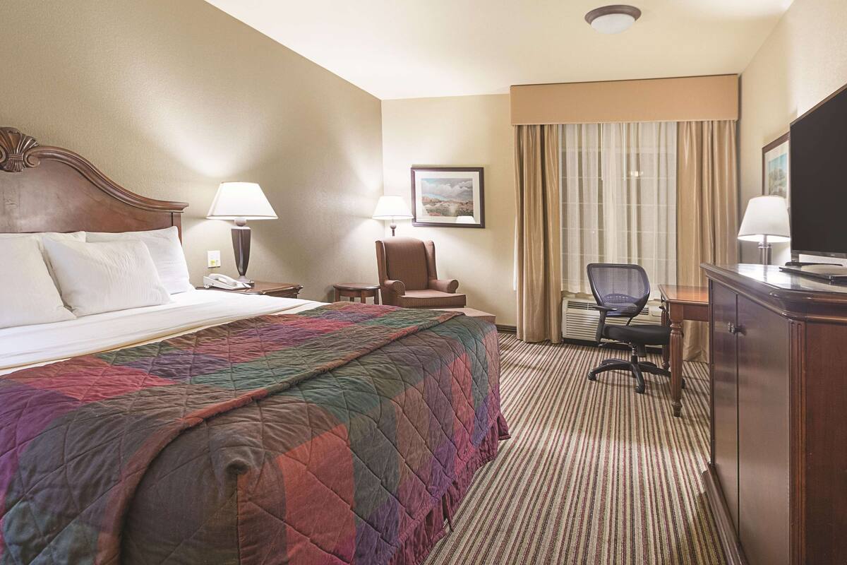 Een hotelkamer met een groot bed, een bureau met stoel, een televisie en een raam met gordijnen.