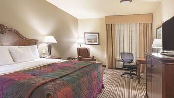 A hotel room with a large bed, a desk with a chair, a television, and a window with curtains.