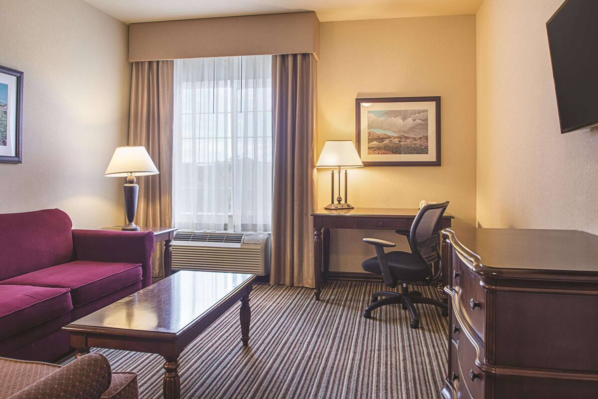 Hotelkamer met een bank, bureau, stoel, lamp, foto aan de muur en een raam met gordijnen.
