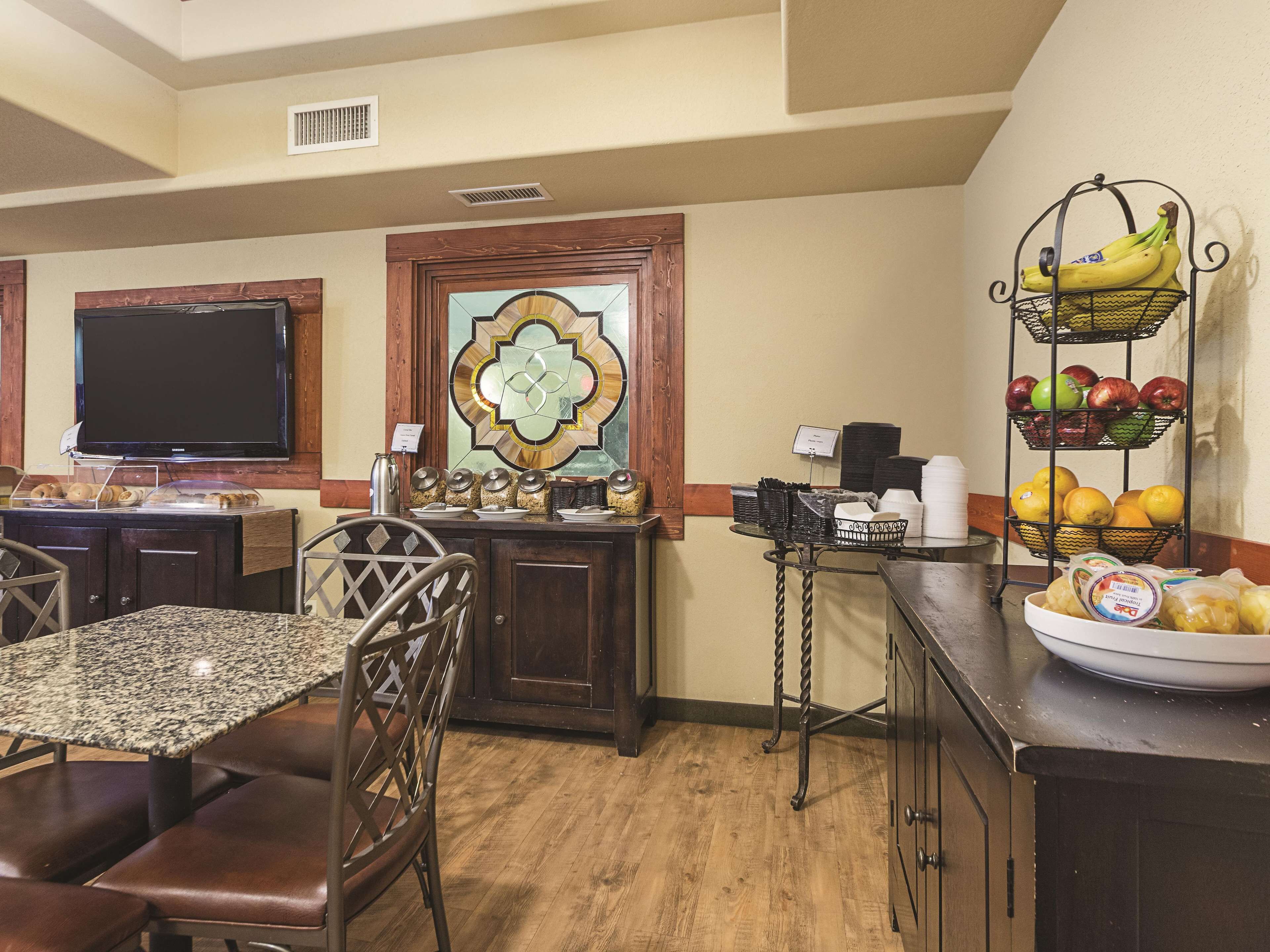 Un espace de restauration d’hôtel avec un buffet, un téléviseur et un présentoir de fruits.