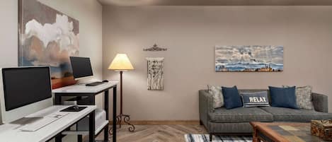 A modern living room with a desk, computer, and a sofa with a 'RELAX' pillow.