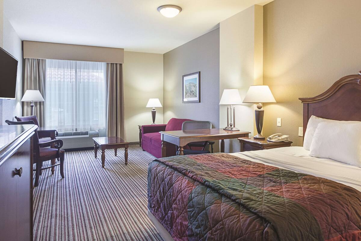 Een hotelkamer met een bed, een bureau, een stoel, een televisie en een raam met gordijnen.