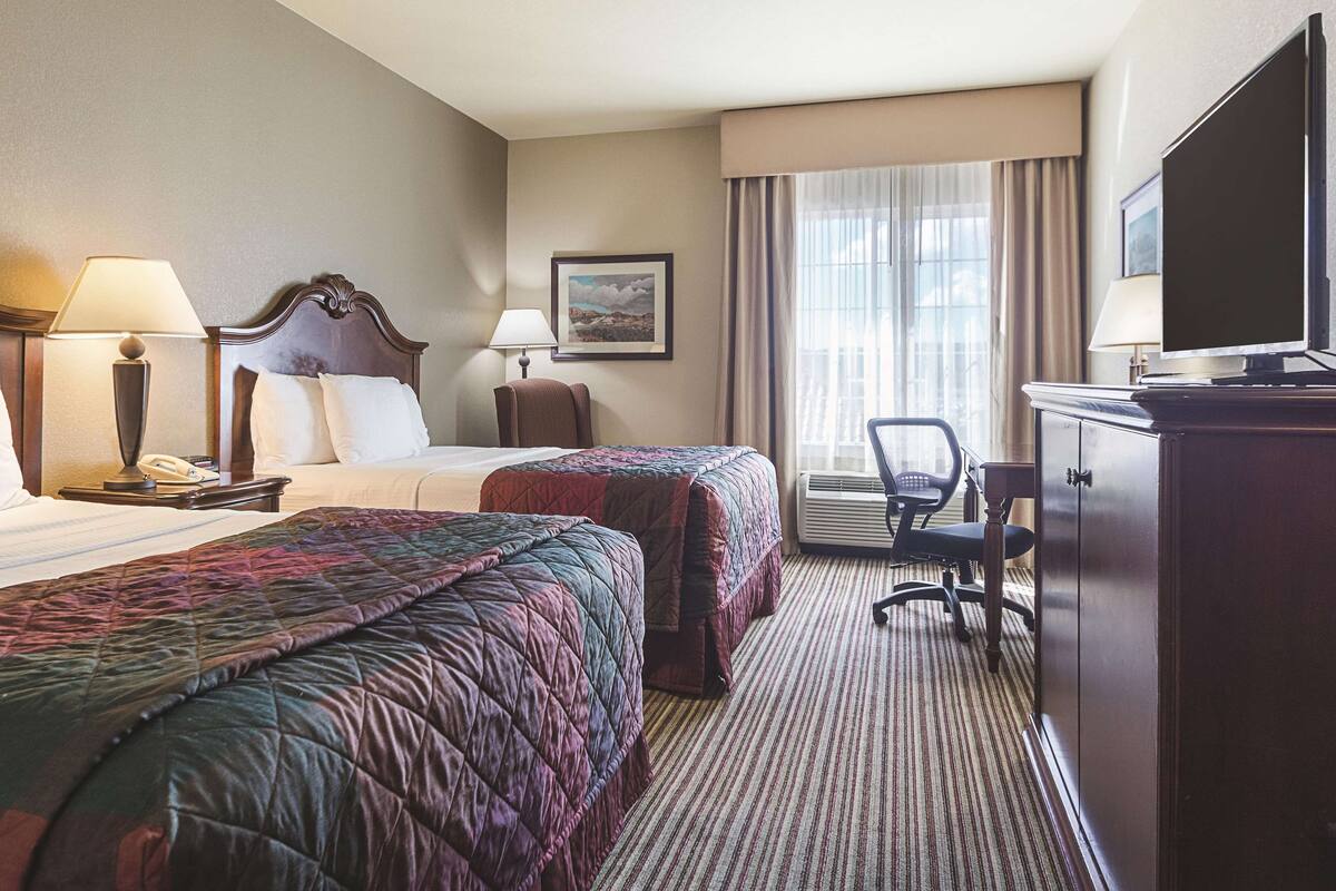 Een hotelkamer met twee bedden, een bureau, een stoel, een televisietoestel en een raam met gordijnen.