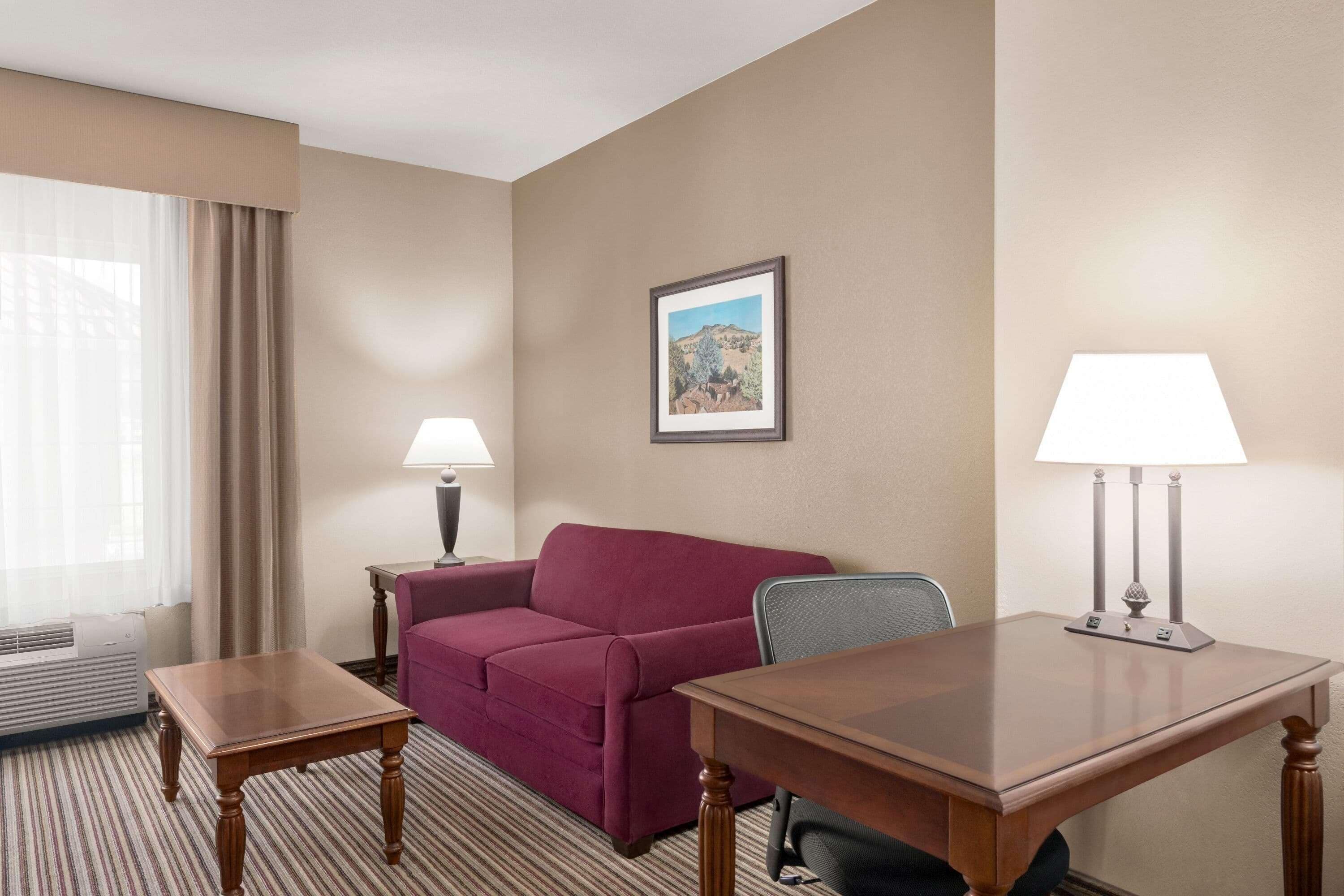 Ein Hotelzimmer mit einem Holztisch, einem roten Sofa, einer Lampe und einem gerahmten Bild an der Wand.