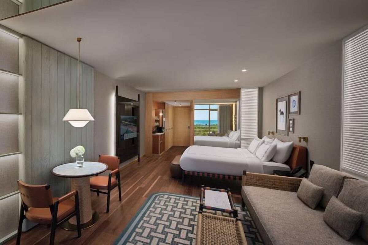 A hotel room with a bed, a sofa, a dining table with chairs, a lamp, and a view of the outdoors.