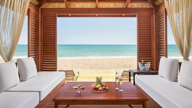 A beachside room with a wooden ceiling, two white sofas, a wooden table with fruit and drinks, and a view of the ocean. - Gloria Serenity Resort - All Inclusive (Serik)