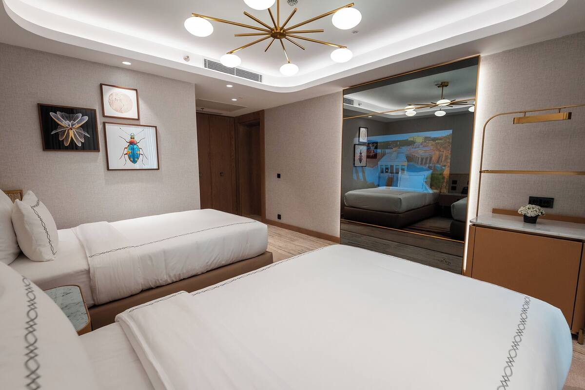 A hotel room with a large bed, a smaller bed, a vanity with a mirror, and artwork on the walls.
