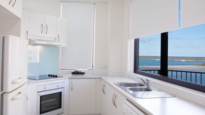 Une cuisine moderne avec des armoires blanches, un four encastré, une plaque de cuisson et une grande fenêtre donnant sur la mer.